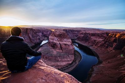Rear view of man sitting at horseshoe bend against sky