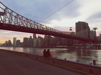 Couple sitting on retaining wall at roosevelt island with queensboro bridge over east river