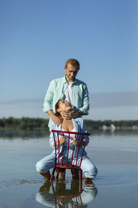 Latin woman sitting in chair in water, looking at caucasian man, male holds, admires female face