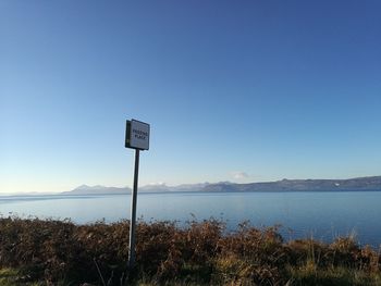 Road sign by sea against clear blue sky