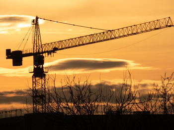 Low angle view of silhouette cranes against sky during sunset