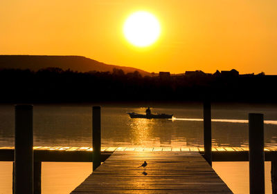 Silhouette pier over lake against orange sky