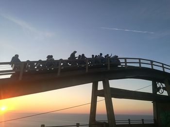 Silhouette bridge over sea against sky during sunset