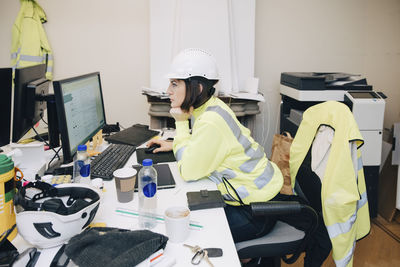 Side view of female engineer sitting with hand on chin while working on computer in office