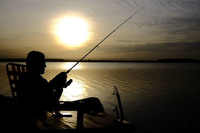 Silhouette man fishing in lake against sky during sunset