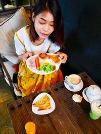 High angle view of young woman holding food in plate while sitting at table