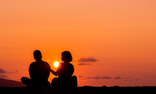 Couple sitting at beach, silhouette in sunset, love and friendship.