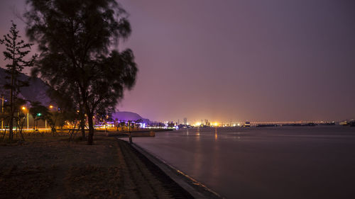 Illuminated street by buildings against sky at night
