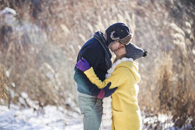Side view of couple kissing while standing on snow covered field