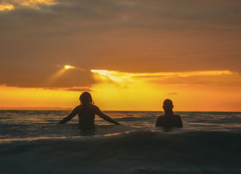 Silhouette woman standing at beach against sky during sunset