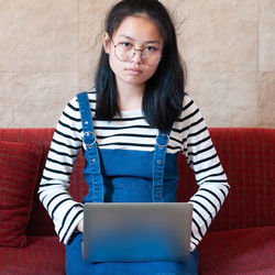 Portrait of young woman using phone while sitting on sofa