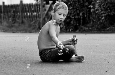 Shirtless boy playing with bubbles on road