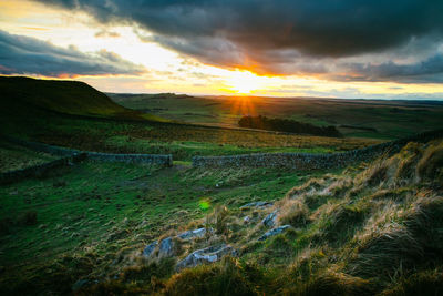 Hadrians wall on field against cloudy sky during sunset