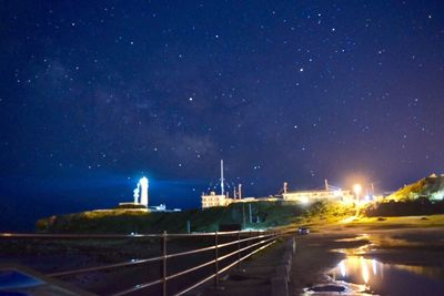 Illuminated street by sea against sky at night