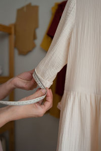 Crop tailor using tape to measure sleeve of handmade white dress while working in studio in daytime