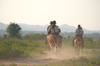 Men riding horse on field against sky