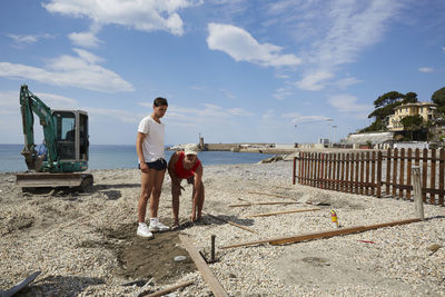 Rear view of men standing at beach against sky