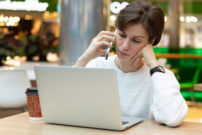 Businesswoman talking on phone while looking at laptop