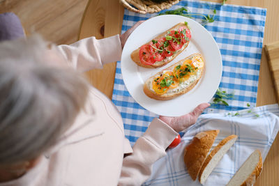 Aged woman holds in her hands a plate with healthy sandwiches with microgreens and vegetables