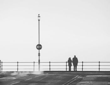 Couple standing on bridge against clear sky