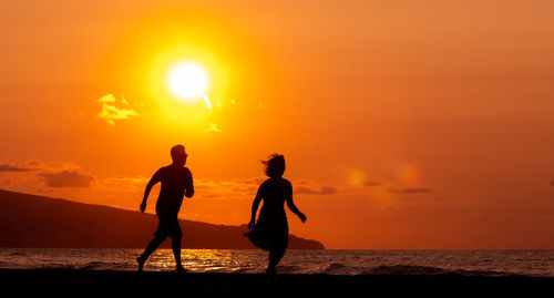 Couple running and having fun at beach, silhouette in sunset, love and friendship.