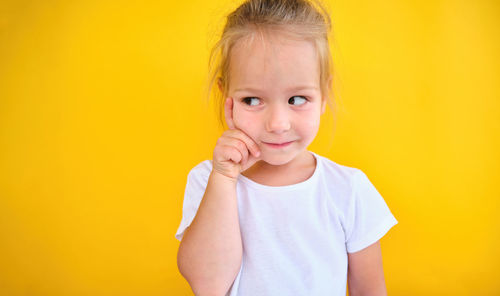 Happy little girl child thinking dreaming many ideas isolated yellow background.