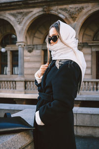 Woman wearing sunglasses standing against built structure