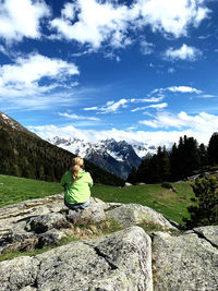 Woman sitting on rock by mountain against sky