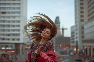 Portrait of woman tossing hair while standing in city