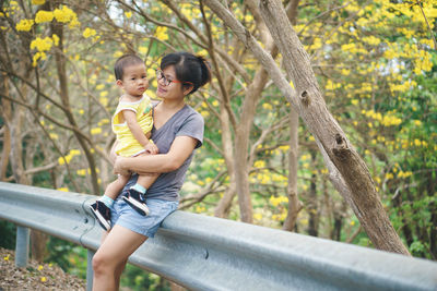 Smiling woman with son leaning on railing in forest