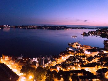 High angle view of illuminated city by sea at night