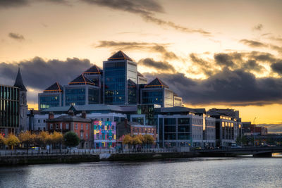 Buildings by river against sky during sunset