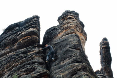 Low angle view of man climbing rock against sky