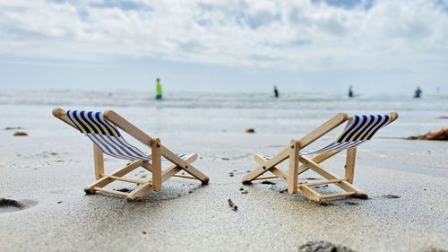 Empty chairs on beach against sky