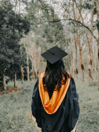 Portrait of woman wearing graduation gown standing on field