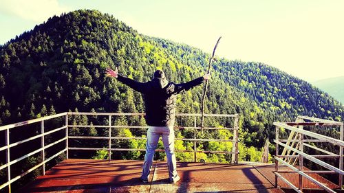 Rear view of man standing by fence against mountain