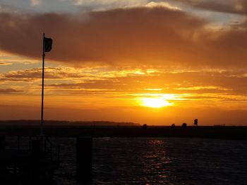 Silhouette street by sea against orange sky