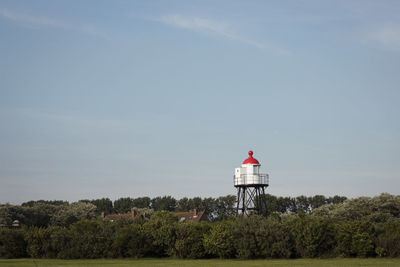 Lighthouse on field by building against sky