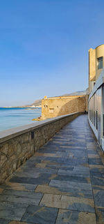 Footpath by sea against clear blue sky