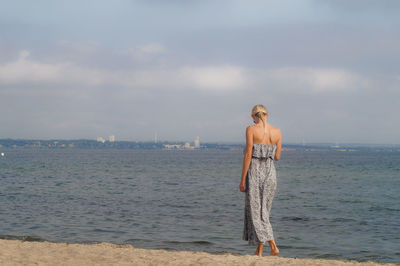 Rear view of woman walking on shore at beach against sky