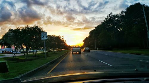 Cars on road against cloudy sky during sunset