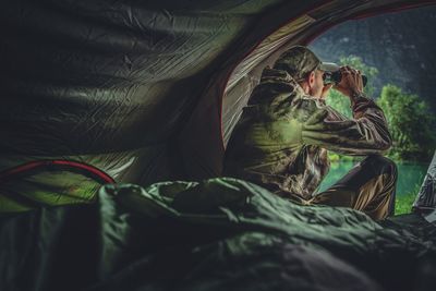 Man looking through binoculars while sitting in tent