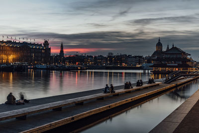 View of illuminated pier over river against cloudy red sky in amsterdam