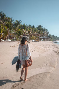 Rear view of woman walking at beach against blue sky