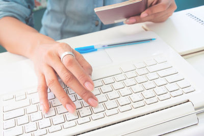 Midsection of woman holding passport while using laptop