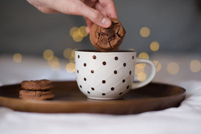 Chocolate cookie with hot milk in cup on wooden tray over glowing lights close up in bed. 