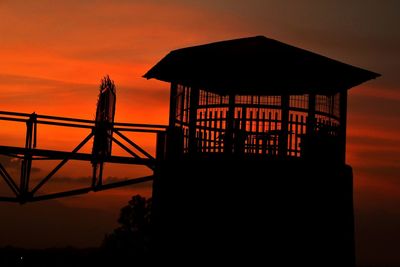 Silhouette built structure by sea against orange sky