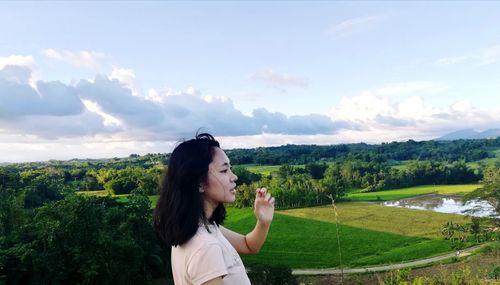 Young woman standing by tree against sky