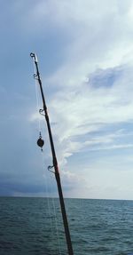 Fishing rod by sea against sky