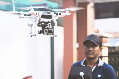 Young man looking at drone flying against building